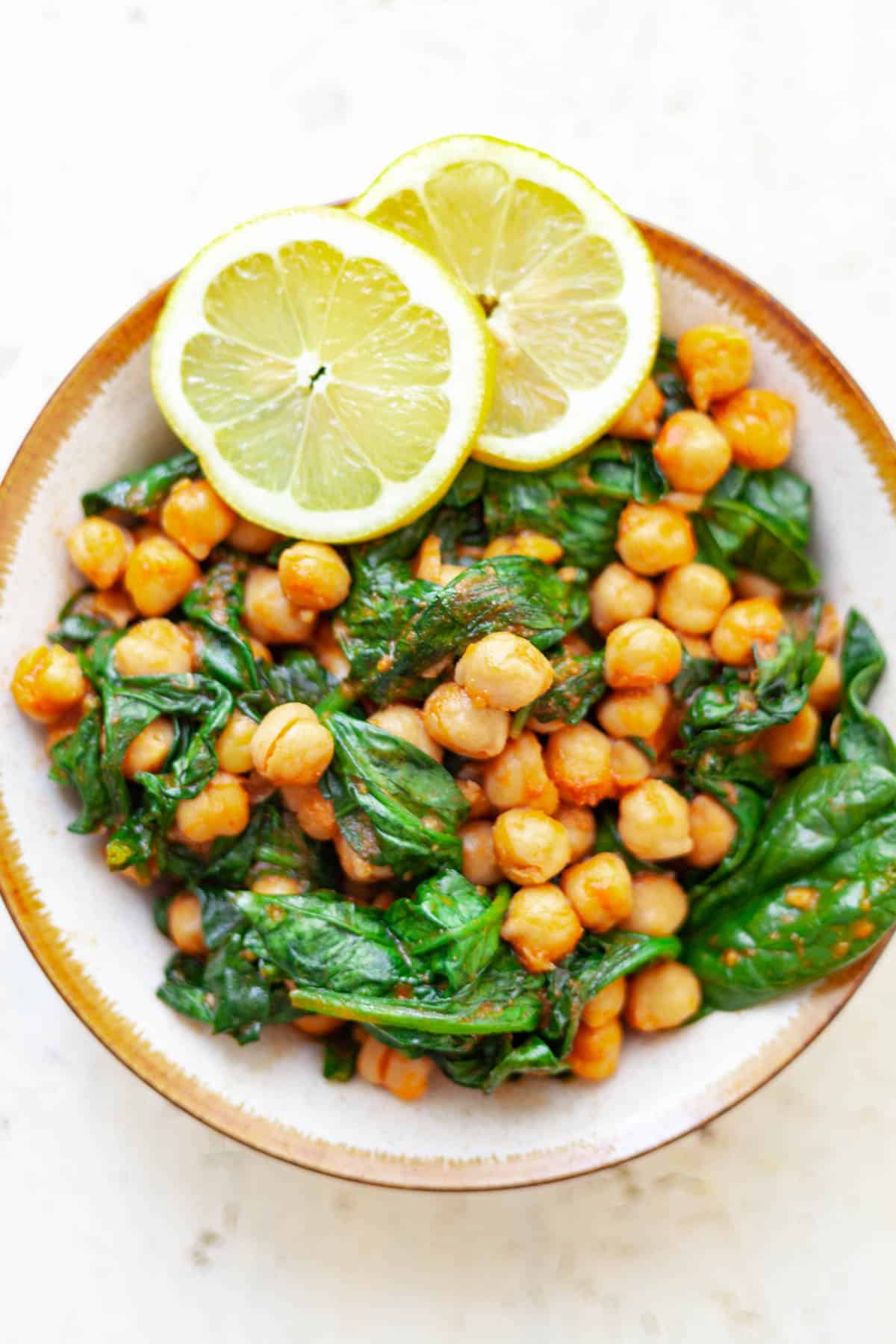 garbanzo beans in a bowl with cooked baby spinach and two slices of lemon