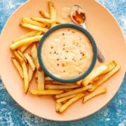 a bowl of red creamy sauce on a plate with french fries