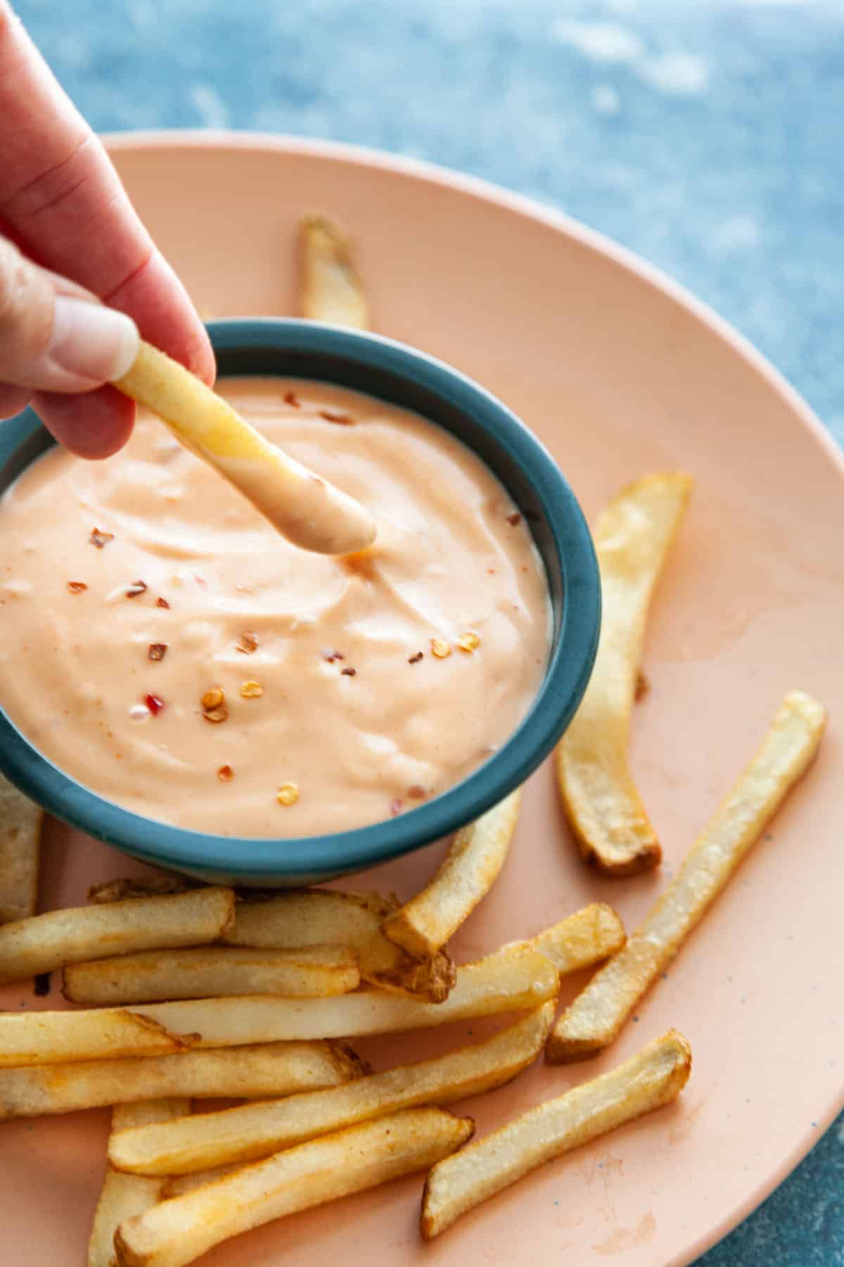 a hand dipping a french fry into sauce