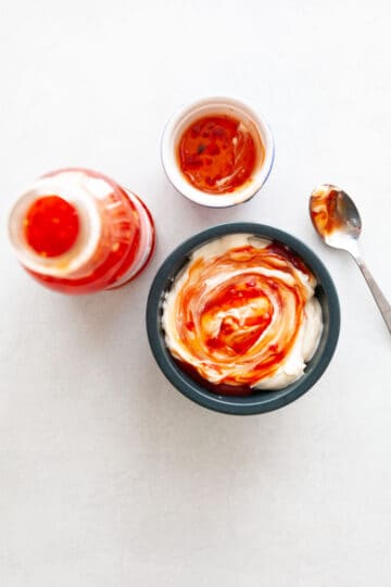 a bottle of red chili sauce next to a bowl of mayonnaise with red chili sauce being stirred into it