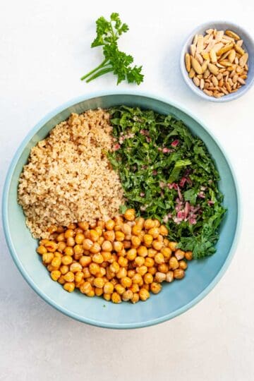 a bowl combining the salad ingredients, like quinoa, kale, chickpeas and dressing