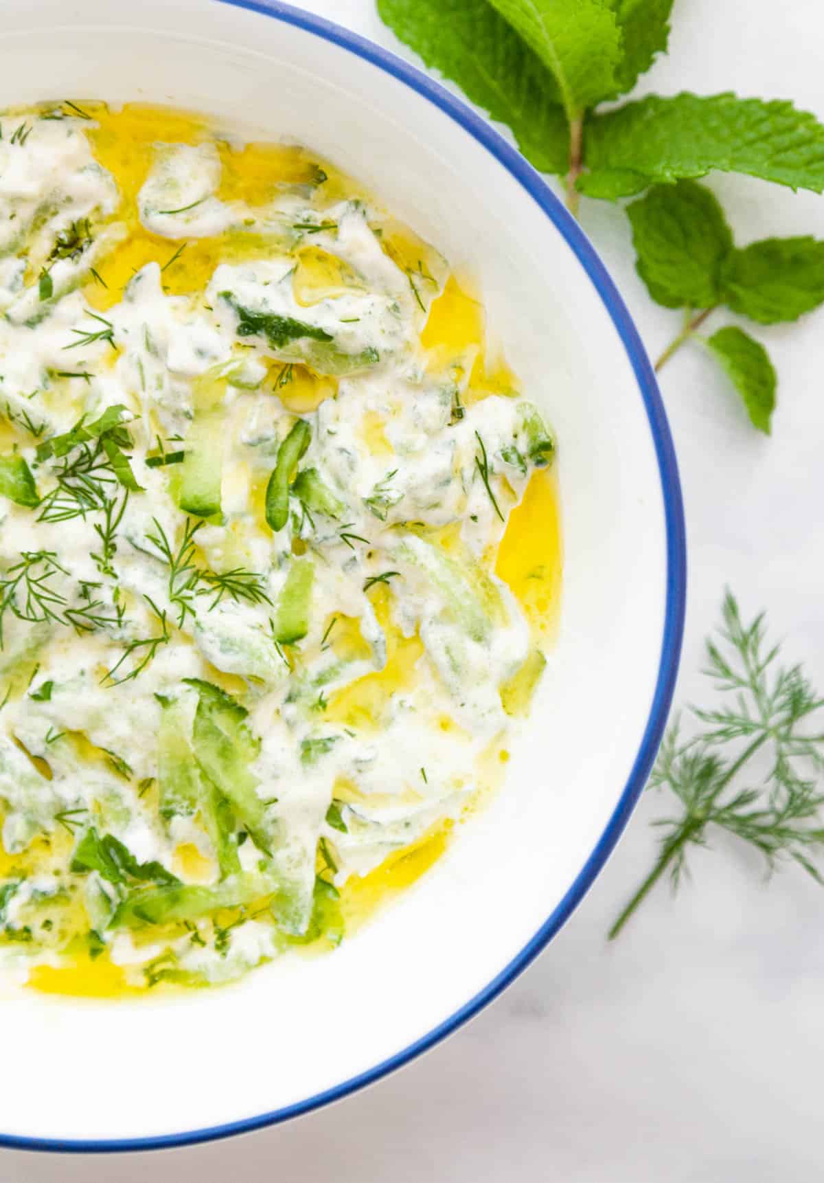 a bowl of sour cream with olive oil drizzled on top and fresh herbs