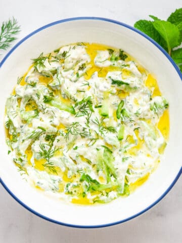 a bowl of sour cream with grated cucumber and fresh herbs