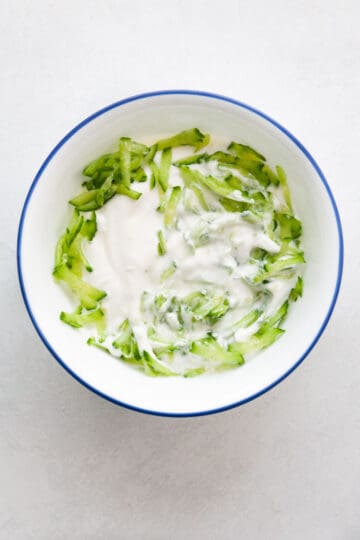 grated cucumber added to a bowl of yogurt