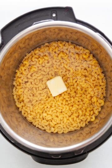 uncooked macaroni, water and a pat of butter in a pressure cooker