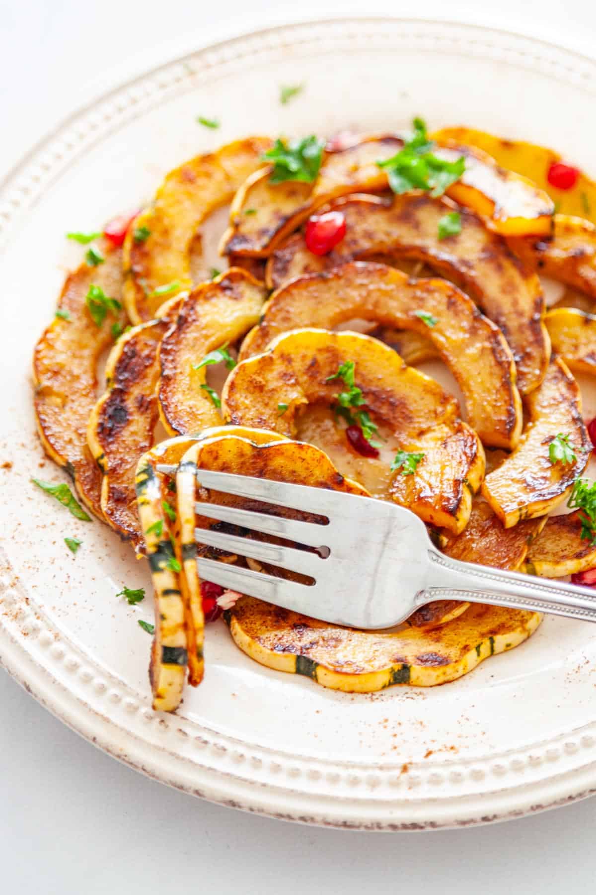 A fork spearing slices of delicata squash on a plate.