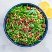 A bowl of arugula quinoa salad sprinkled with dried cranberries and pieces of pecans.