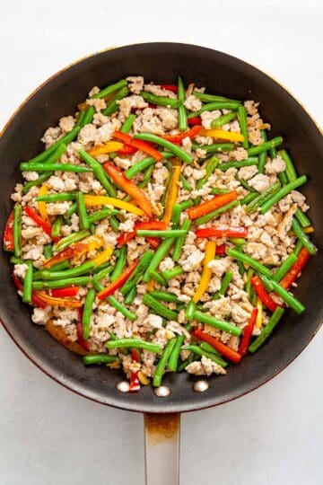 Ground chicken, green beans and sliced bell peppers in a skillet.