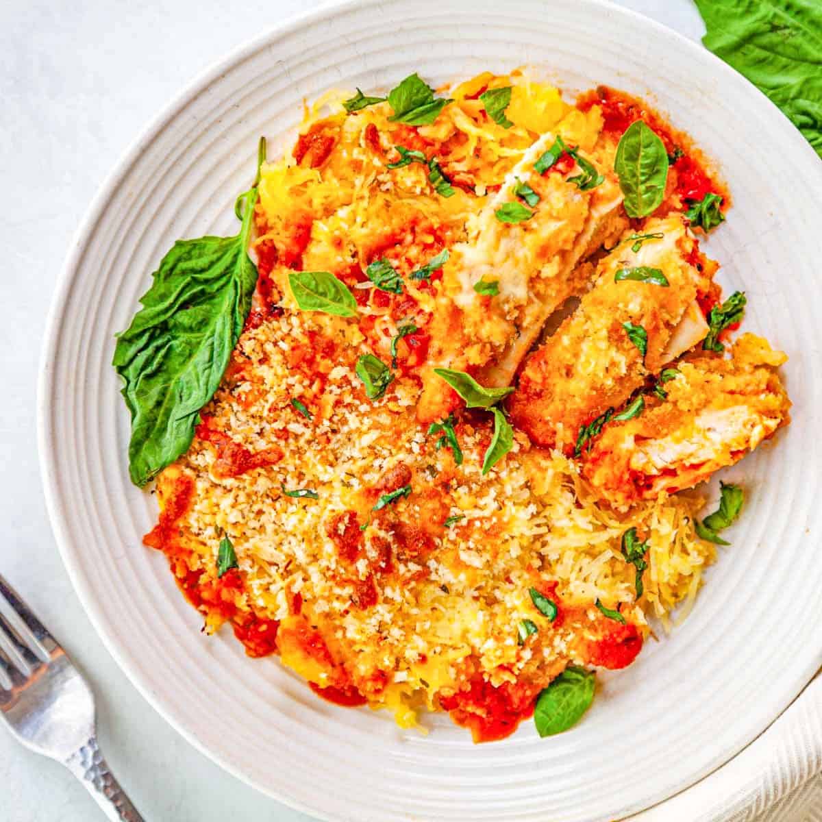 A plate of sliced chicken breast over spaghetti squash with marinara and melted cheese.