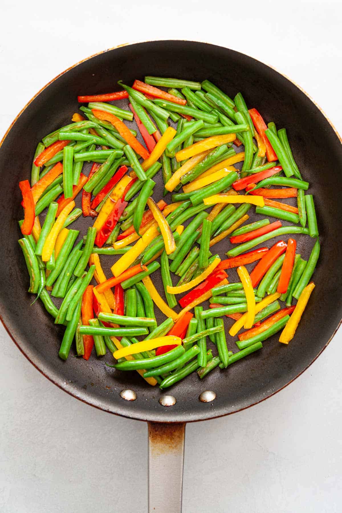 Sliced green beans and bell pepper in a saute pan.