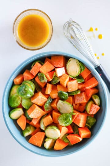 A bowl of cut Brussels sprouts and sweet potatoes in a bowl tossed with maple dijon vinaigrette.