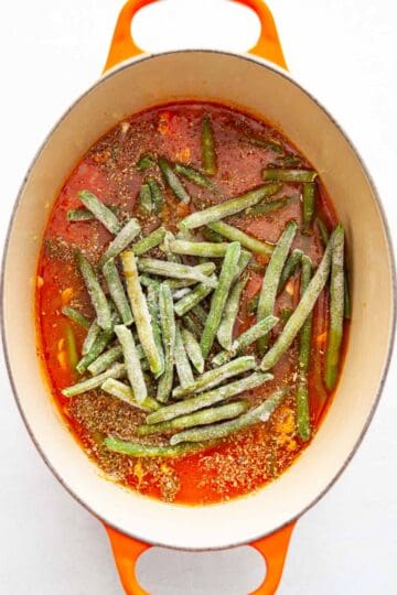Frozen greens beans in a Dutch oven with tomato-based broth.