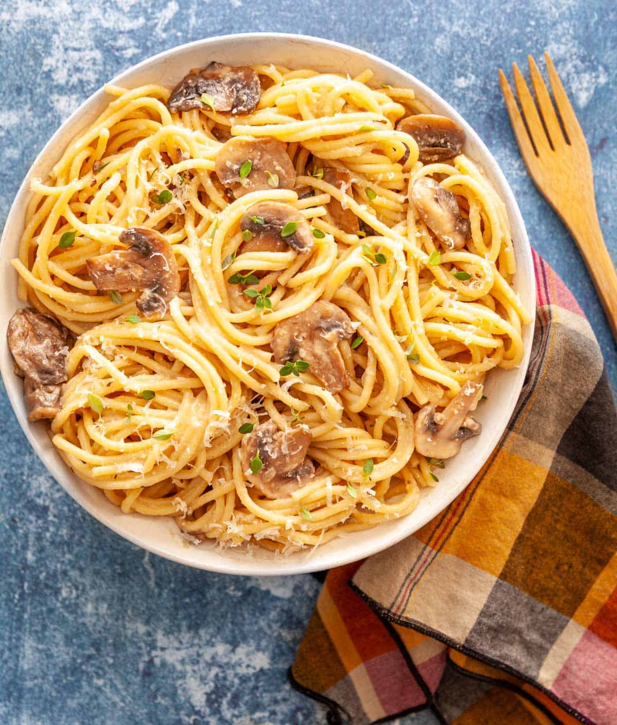 A bowl of spaghetti noodles with mushrooms, grated parmesan and fresh thyme.