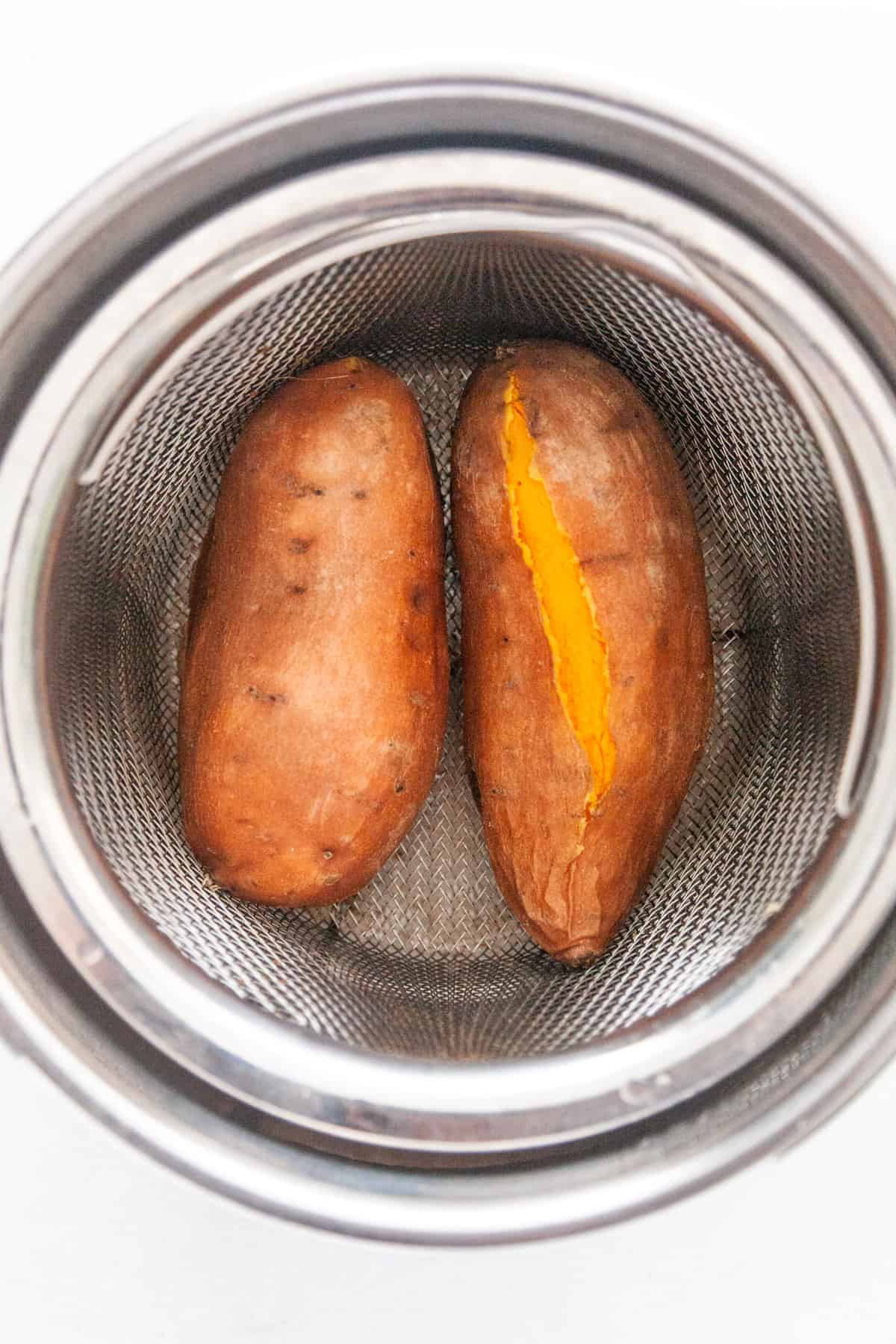 Two whole sweet potatoes in a pressure cooker steamer basket.