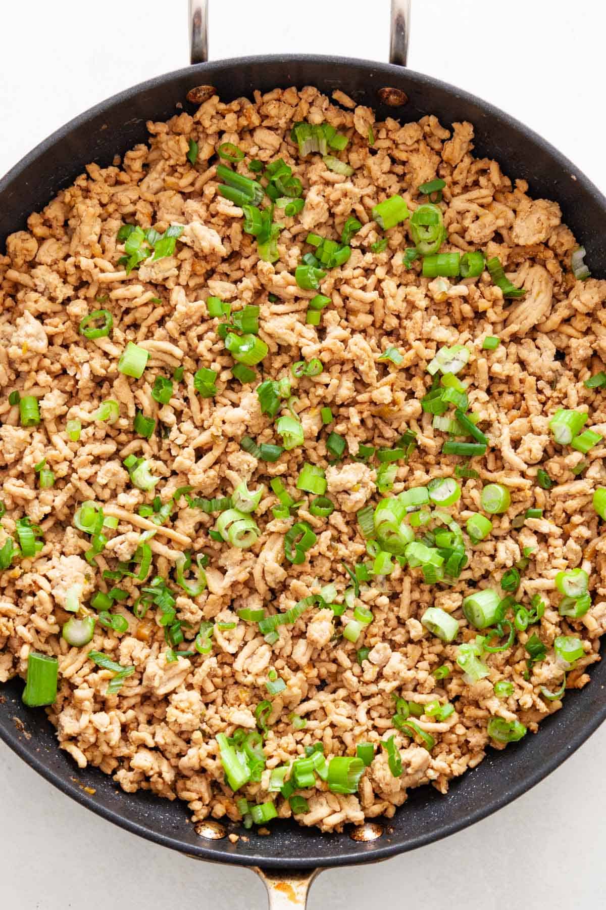 Ground meat and green onion in a skillet.