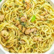 A bowl of spaghetti with pesto and canned tuna.